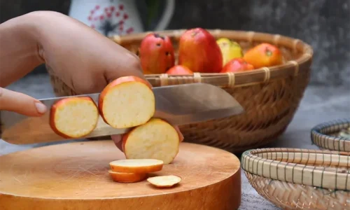 Cắt lát trái điều trên một đế gỗ, có rổ trái điều ở phía sau